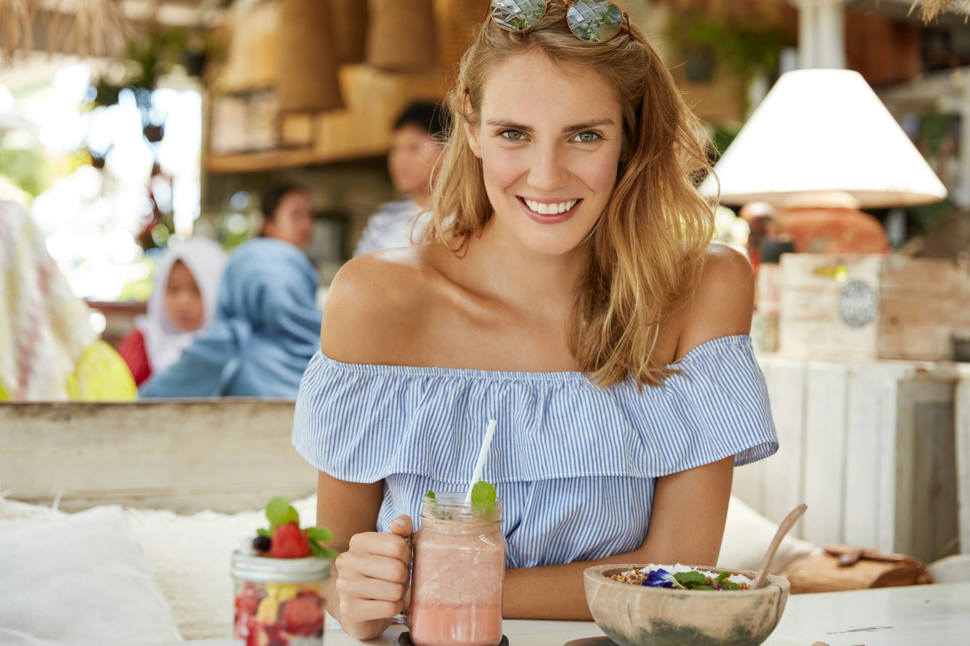 Pretty young woman in sylish blouse, drinks shake, eats salad, sits at cafeteria, smiles happily, sp